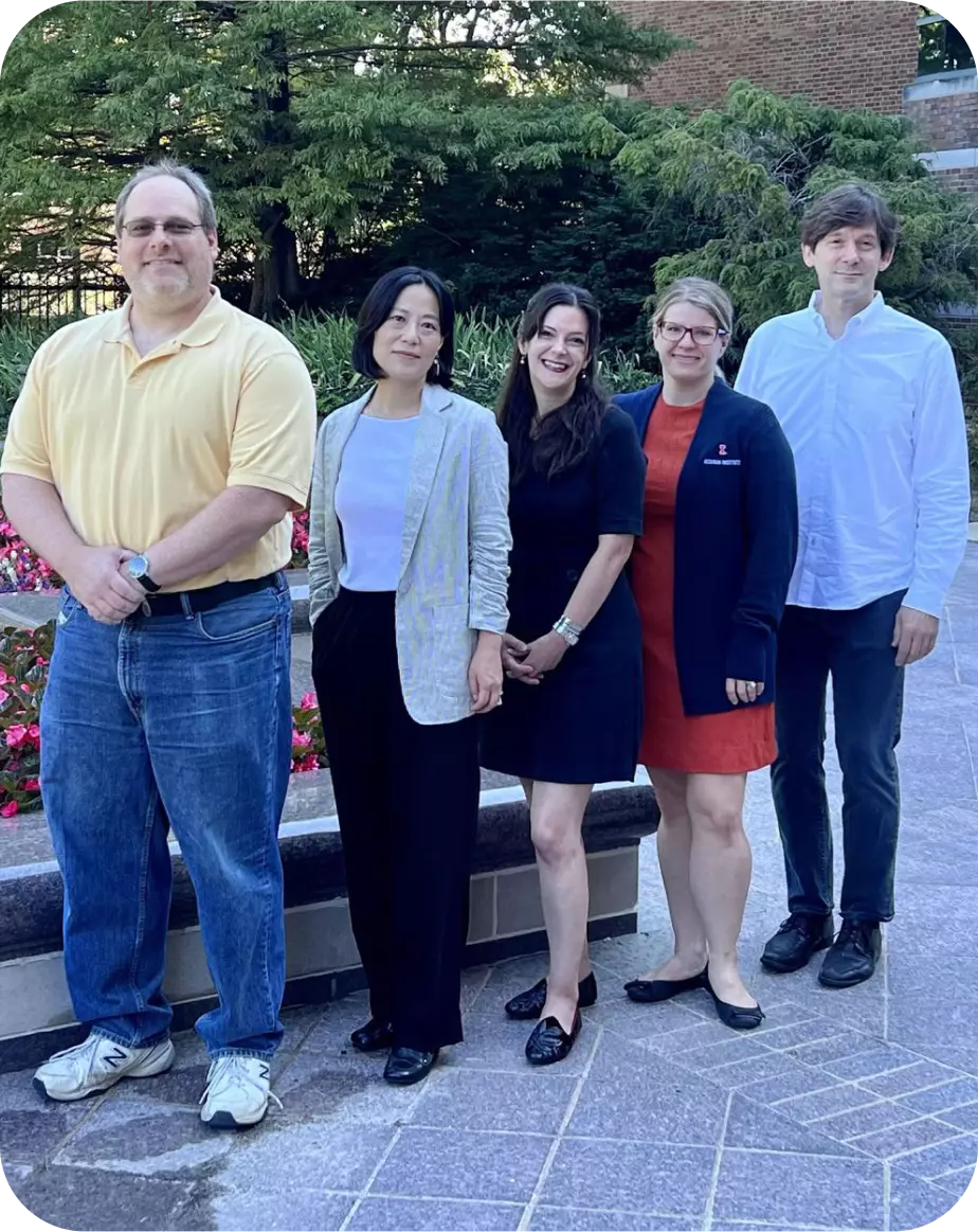 Five people standing in front of a raised garden. Starting from the left: a man in a yellow polo, a woman in a lavendar shirt with a gray blazer, a woman in a navy dress, a woman in a coral dress with a navy blazer, a man in a light blue oxford shirt