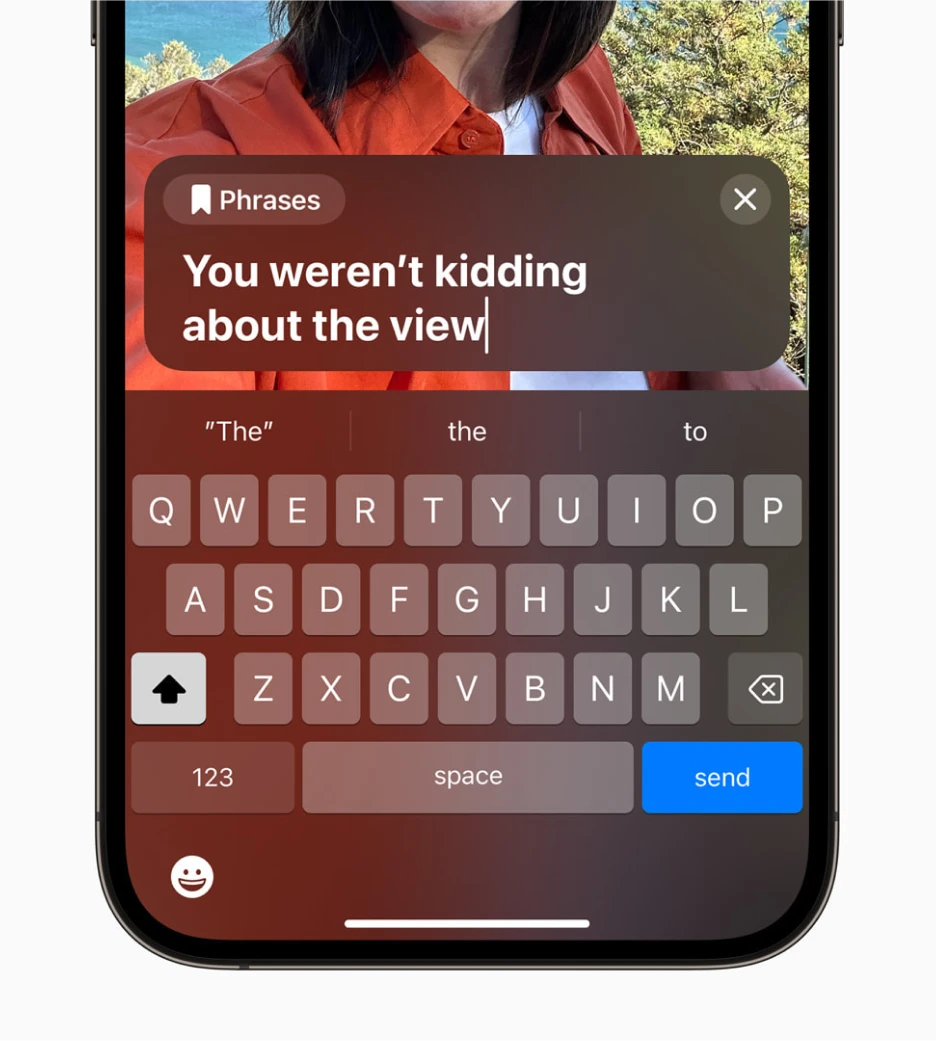 A phrases modal is overlayed on top of a video call showing the phrase `You weren't kidding about the view` and the iOS keyboard below that.