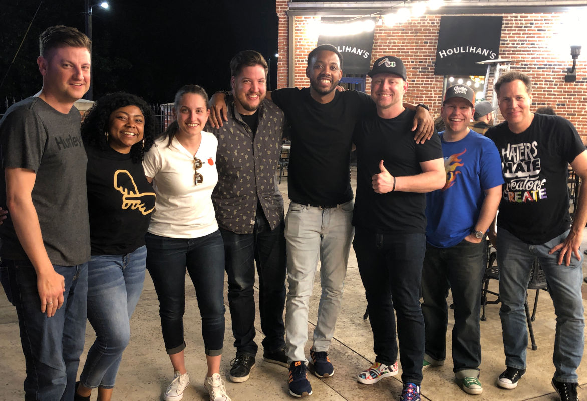 Eight people from a design conference standing in front of a bar toasting to a good conference