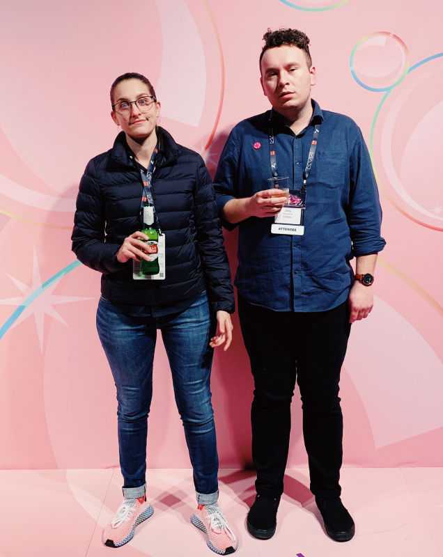 Two people posing at design conference in front of a stylized pink backdrop
